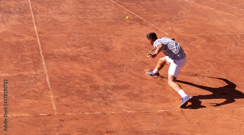 Overhead view of tennis player in action and his shadow on red clay tennis court. Young man plays tennis on the court. Sports background. Banner, copy space for text © Elena