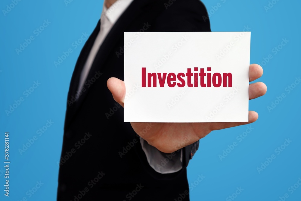 Investition. Geschäftsmann im Anzug zeigt Karte mit Text. Mann isoliert vor Hintergrund (blau) Investition. Geschäftsmann im Anzug zeigt Karte mit Text. Mann isoliert vor Hintergrund (blau)