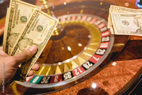 Casino. Dollars in the hands of a gamer player person on the background of a roulette table and a game table. Gambling. Cash game. People place bets in casinos background