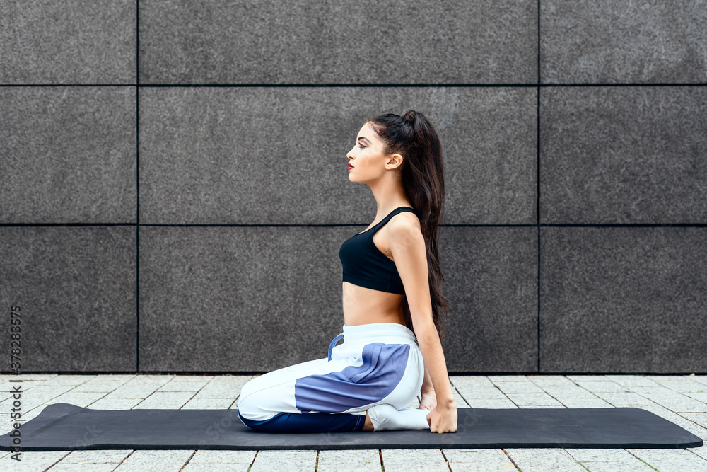 Fototapeta premium teenage girl sit on mat outdoors in urban city with sportswear and braided hair relaxing and meditating after yoga workout while concentrating on natural inner peace