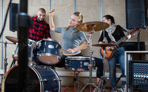 Music garage band with expressive laughing girl drummer rehearsing in sound studio