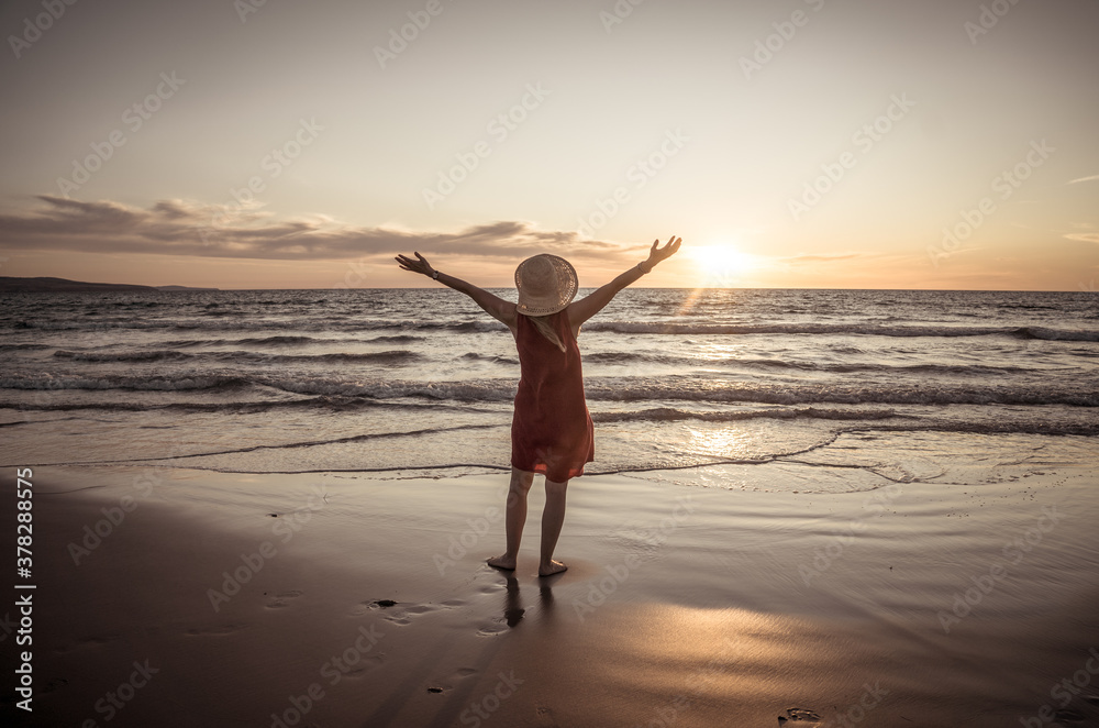 Woman in red with arms outstretched by the sea at sunrise enjoying freedom and life