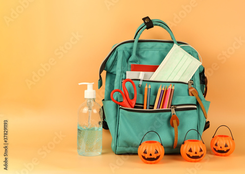 Student backpack , medical mask , alcohol gel and halloween pumpkin bucket on orange background with copy space. Education ,COVID-19 prevention ,Halloween and new normal concept.