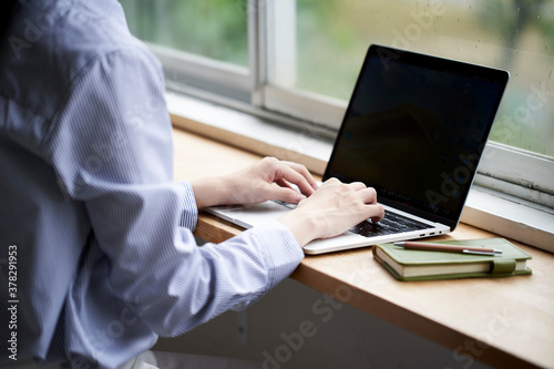 窓際でパソコン操作をする若い女性