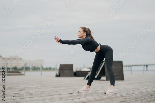 young fitness girl brunette athlete doing sports doing exercise leans forward . sporting a black suit.