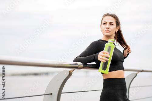 portrait of a female athlete of European appearance stands and holds a bottle of clean water for drinking. quenches your thirst after a sports workout. time morning the weather is good