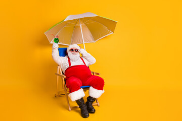 Full size photo of white grey hair bearded santa claus sit chaise-lounge raise alcohol glass x-mas christmas eve noel time relax wear hat pants isolated bright shine color background