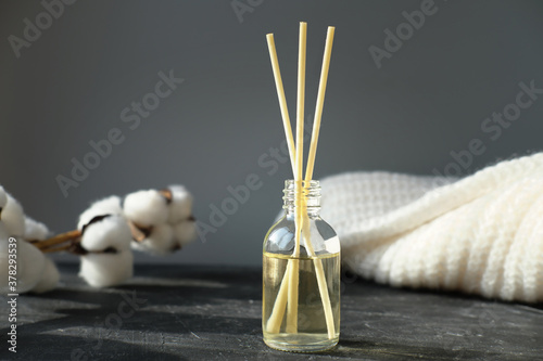  hygge and aromatherapy concept. aroma reed diffuser, branch of cotton and white sweater on grey table at home. minimal style composition. winter and autumn mood