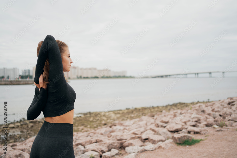 He goes in for sports against the background of the city, stretches his arms behind his back. portrait of a woman of Caucasian appearance in black tight sports comfortable clothing. time the morning. He goes in for sports against the background of the city, stretches his arms behind his back. portrait of a woman of Caucasian appearance in black tight sports comfortable clothing. time the morning.