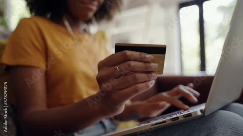Close-up shot of an african american woman holding a credit card in her hand doing internet banking using laptop