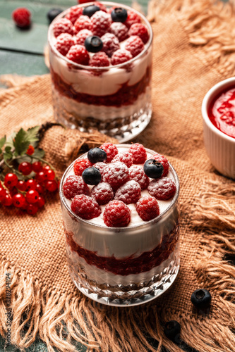 Healthy raspberry fruit dessert with skyr yogurt, granola layered in jar surrounded by ingredients, Vegetarian breakfast, fresh raspberries and blueberries yoghurt