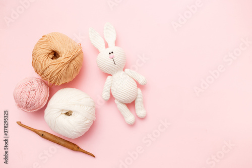 White and brown knitting wool, rabbit amigurumi and crochet hook on pink pastel background. Top view, flat lay, copy space photo