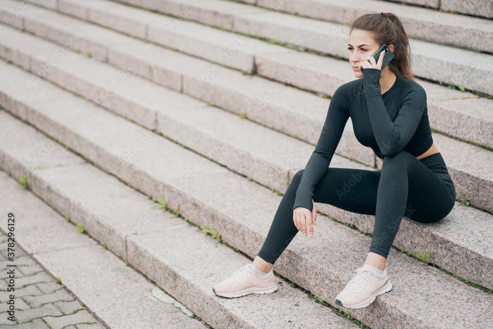 portrait of a young woman of athletic build with a brunette smile on her face. sitting on the steps in a beautiful black sports clothes portrait of a young woman of athletic build with a brunette smile on her face. sitting on the steps in a beautiful black sports clothes
