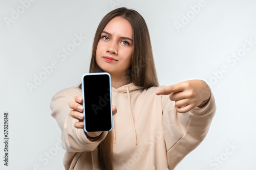 Portrait of pretty girl pointing finger at blank screen mobile phone isolated over white background