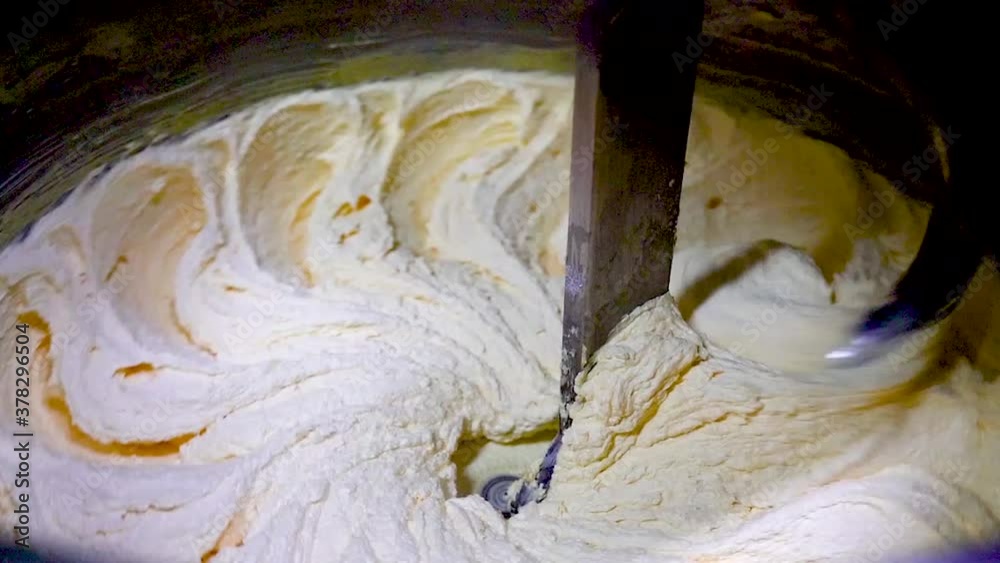 Closeup of butter being whipped in large industrial mixer.