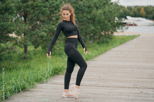 holding a skipping rope brunette woman of European appearance in sports comfortable clothes black. stands posing for the camera. good mood