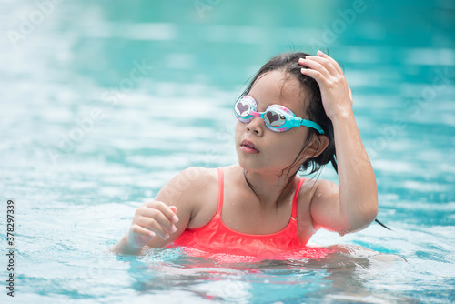 smiling child wearing swimming glasses in swimming pool. little girl playing in outdoor swimming pool on summer vacation on tropical beach island. child learning to swim in pool of luxury resort.