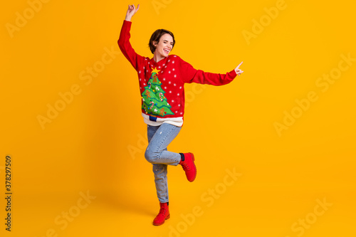 Full size photo of positive cheerful girl dance x-mas newyear party wear christmas tree decor sweater boots denim isolated over bright shine yellow color background