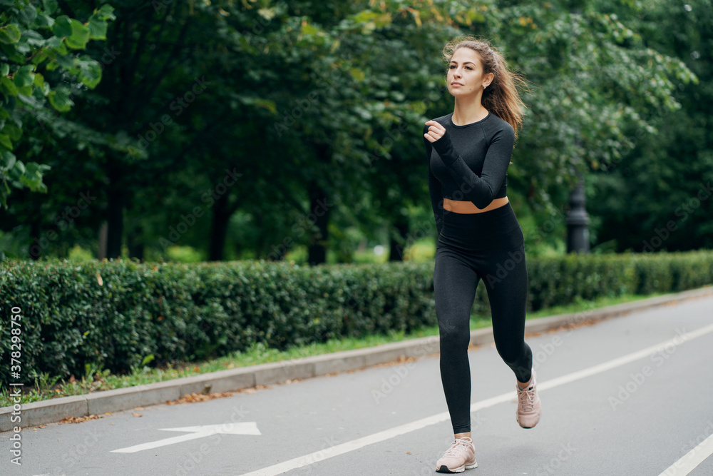 running sports on a cross-country road. portrait of a confident brunette woman of Caucasian appearance. stylish tight comfortable clothing. nice weather summer day