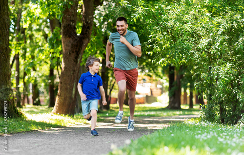 Fototapeta Naklejka Na Ścianę i Meble -  family, fatherhood and people concept - happy father with little son compete in running at summer park
