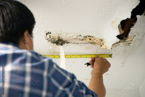 Hole damaged in ceiling house from pipes water leakage with worker repair and fixing ceiling panels. Office building or house problem from plumber system repairman service concept.