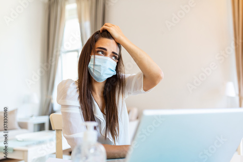 Woman sitting alone in her office and coughing as she suffers from a cold. Medical mask and hand disinfectant and stressed woman. Shot of a businesswoman working in her office while she is sick.