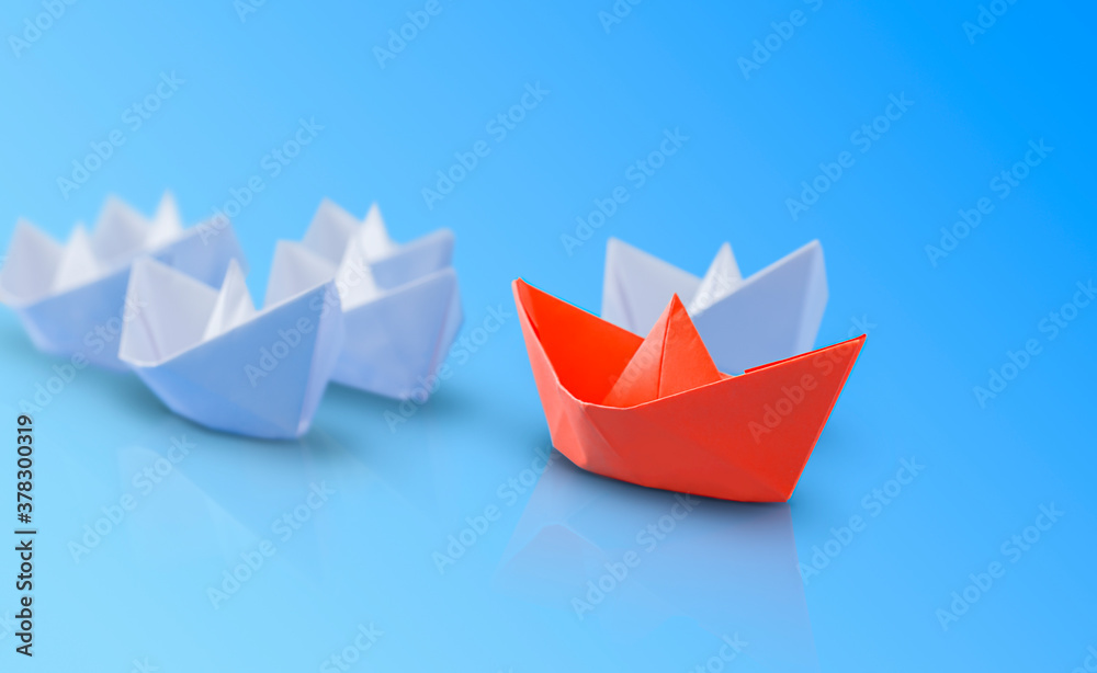 Fototapeta premium red paper boat in front of the white ones. blue background