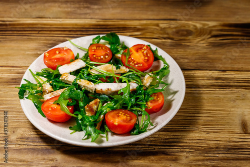 Tasty salad of fried chicken breast, fresh arugula and cherry tomatoes on wooden table