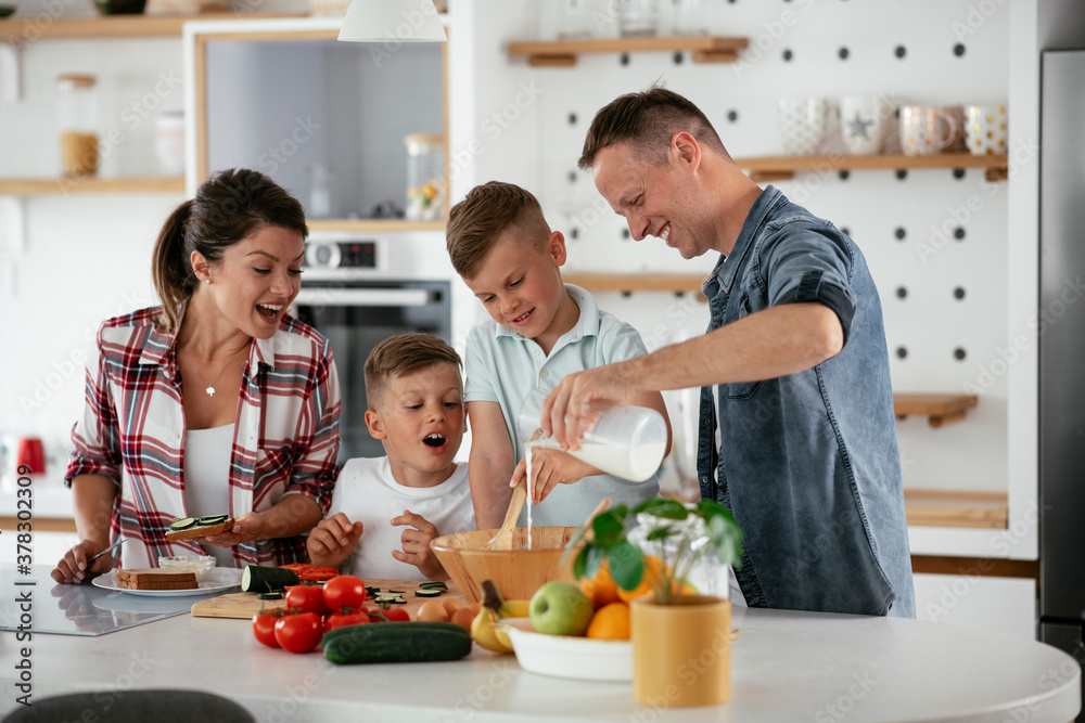  Mother and father making breakfast with sons. Young family preparing delicious food in kitchen