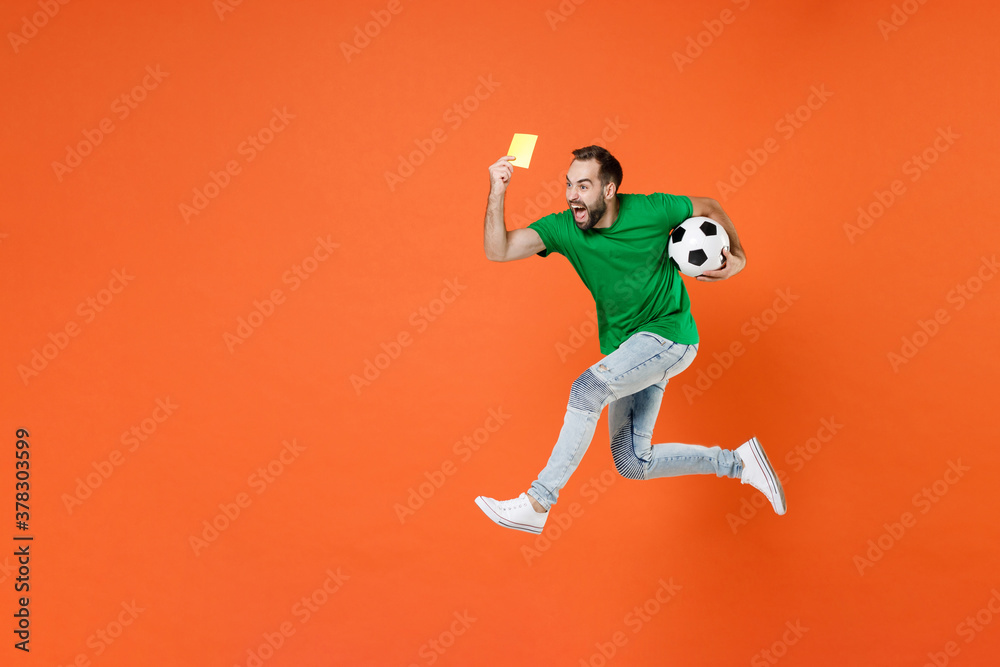 Full length portrait screaming man football fan in green t-shirt support favorite team with ball jumping propose player retire from field isolated on orange background. People sport leisure concept.