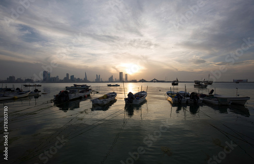 Boats parked at the coast with backdrop of Bahrain skyline at sunset