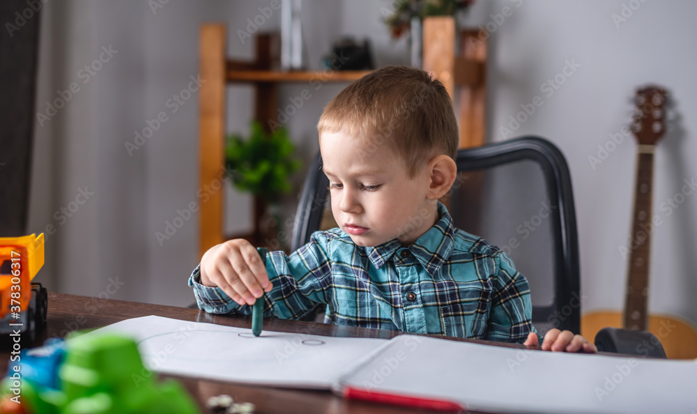 Cute child boy draws with chalk on paper in an album at the table. Preschool education and development of creativity Cute child boy draws with chalk on paper in an album at the table. Preschool education and development of creativity