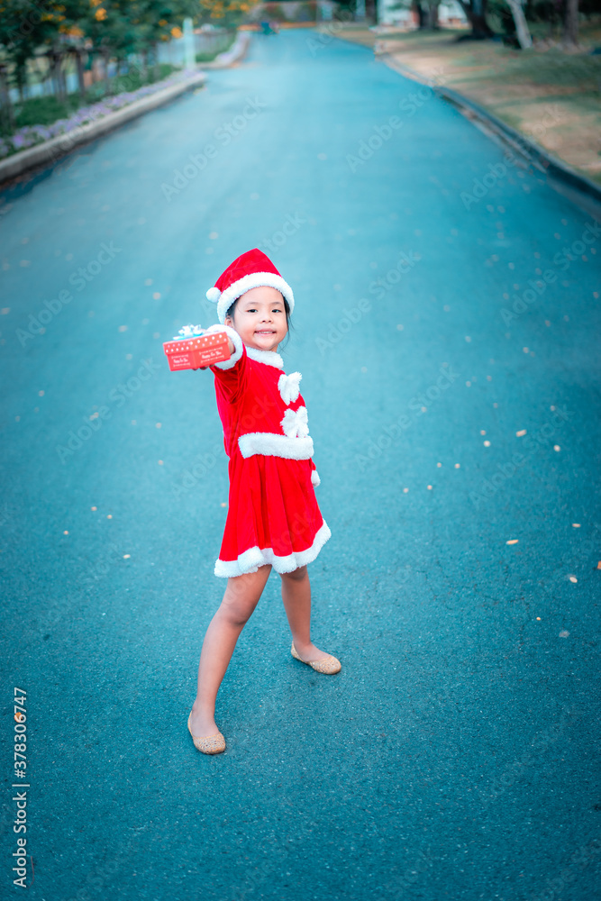Obraz premium little asian girl in red Santa Claus costume with present box on the road
