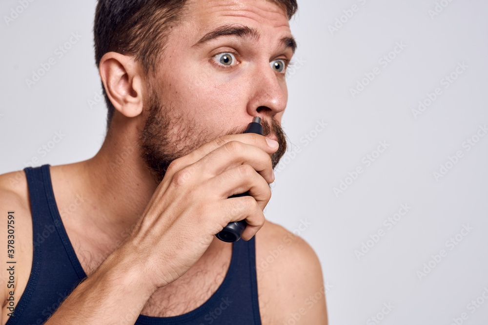 A man with a machine for removing hair from a nose in a black T-shirt light background body care