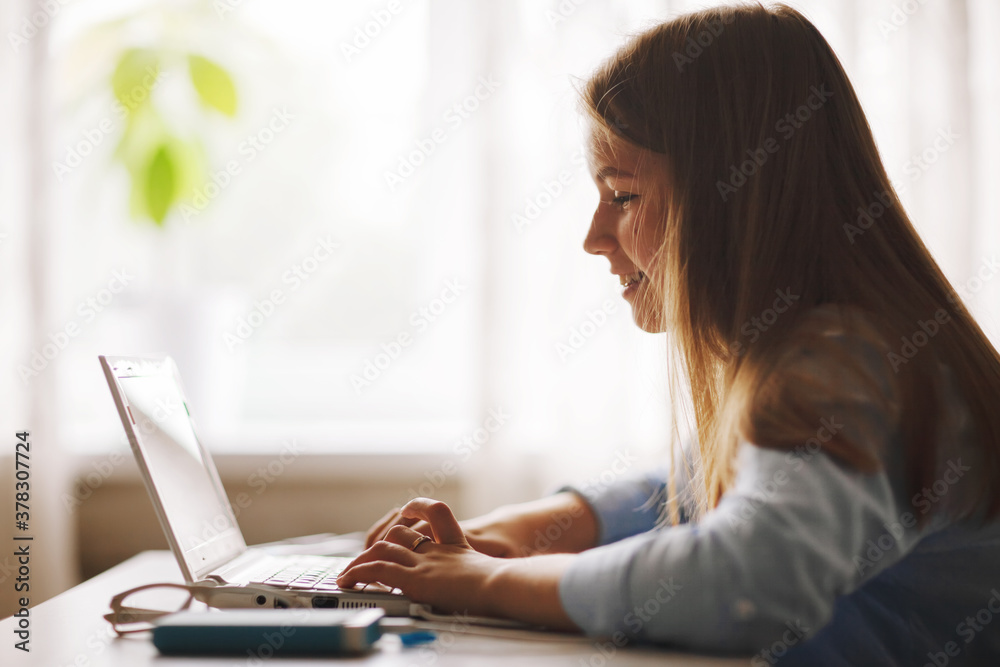 Teenage girl wearing headphones sitting at table and doing homework by video conference using laptop, online education, distance learning, technology concept Teenage girl wearing headphones sitting at table and doing homework by video conference using laptop, online education, distance learning, technology concept