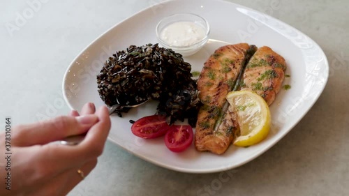 dish with fish and black rice on a white plate. woman eating fish dinner in a restaurant