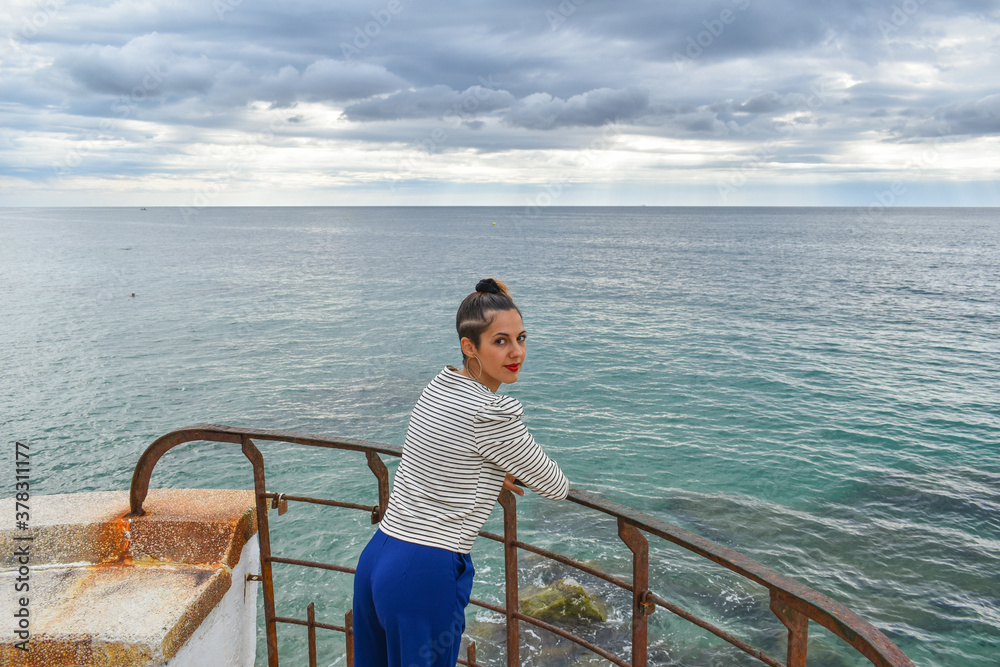 Woman leaning from an iron railing looking out to sea.