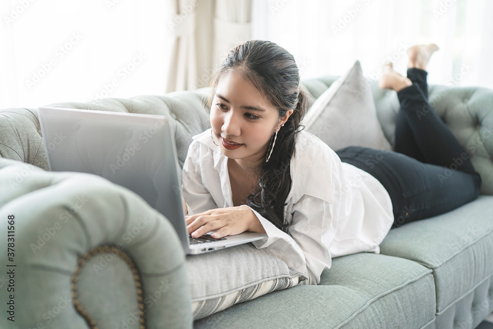 Happy casual beautiful Asian woman working on a laptop sitting on the couch in the house. Happy casual beautiful Asian woman working on a laptop sitting on the couch in the house.