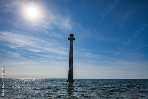 Abandoned tilt lighthouse "Kiipsaare tuletorn" on Baltic Sea. Estonia. Saaremaa island. Rippled water and blue sky with sun and nice clouds. Estonia, Saaremaa, Harilaid nature reserve.