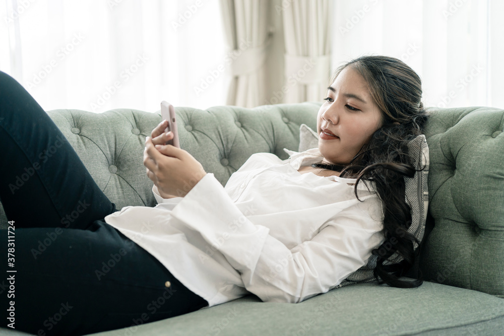 Happy casual beautiful Asian woman working on a laptop sitting on the couch in the house. Happy casual beautiful Asian woman working on a laptop sitting on the couch in the house.