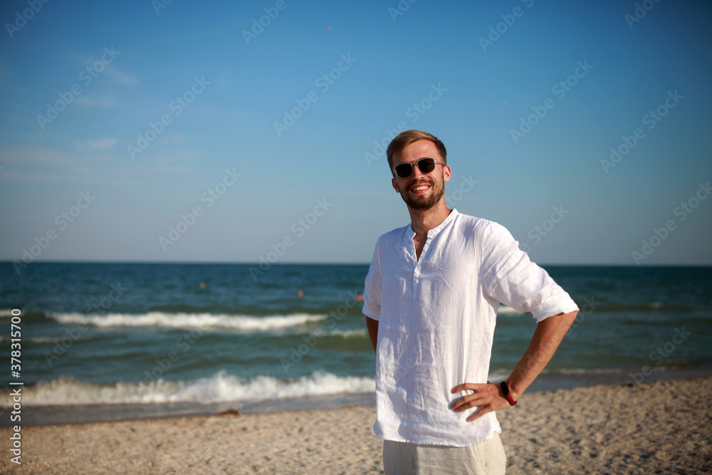 Young smiling man stands on beach against sea and sky background. Young smiling man stands on beach against sea and sky background.