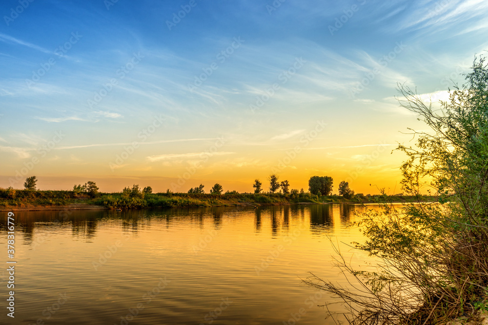 Picturesque summer landscape with riverbank at sunset. Calm plain river, reflection in water. Wonderful nature, beautiful natural background. Akhtuba river, Astrakhan region, Russia