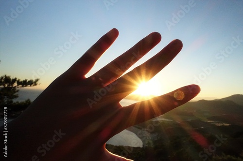 立石山から見る糸島のまぶしい朝日に手をかざす