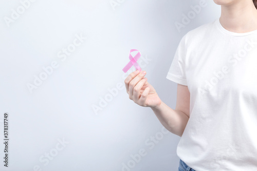 World Breast cancer day concept. Woman in white T-shirt holds pink ribbon in her hand. October Breast Cancer Awareness month. Copy space