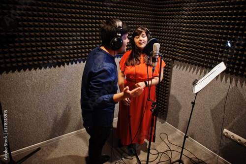 Young asian duet singers with microphone recording song in record music studio. photo