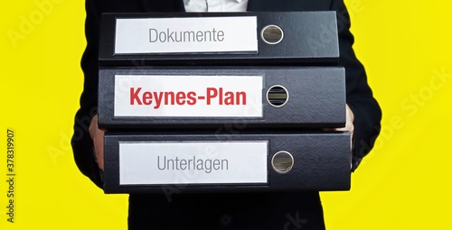 Keynes-Plan. Mann trägt Stapel Ordner. Aktenordner haben Beschriftung mit Text. Hintergrund gelb. photo