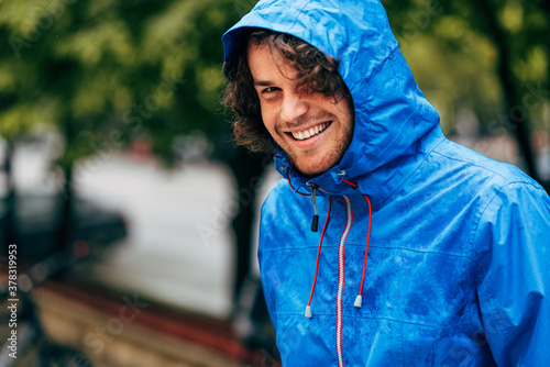 Φωτογραφία Closeup portrait of a happy man smiling, wearing blue raincoat during the rain outside