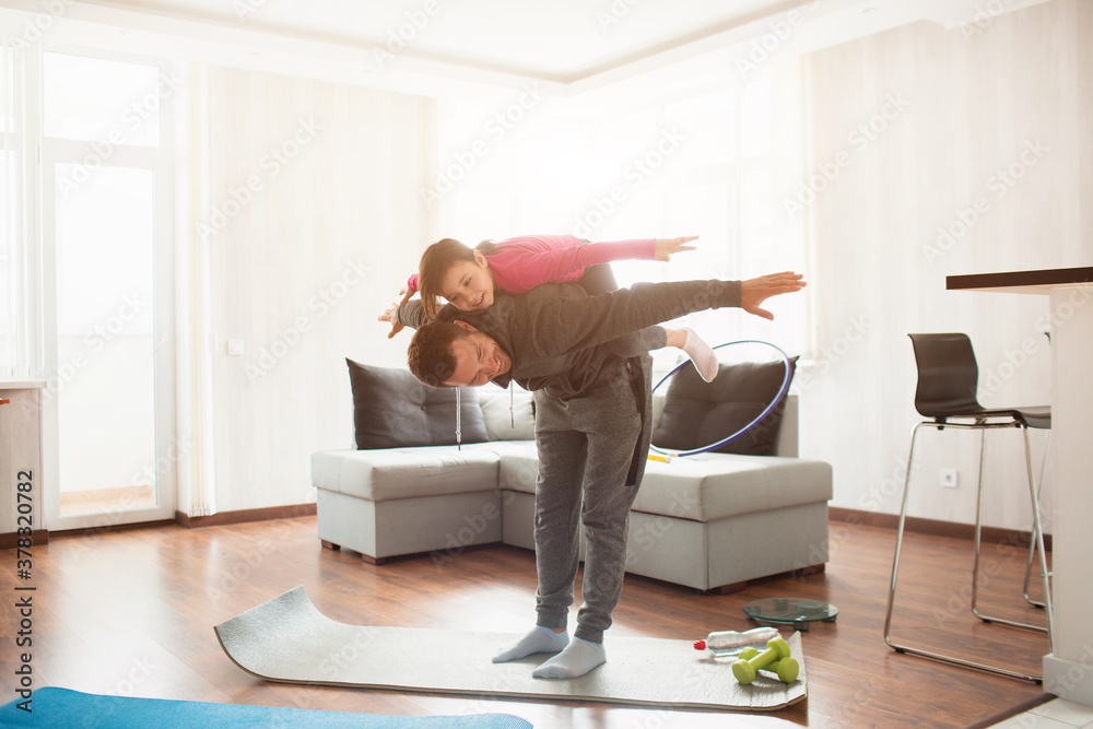 father and daughter are training at home. Workout in the apartment. Sports at home. Daughter climbed on her back and has fun.