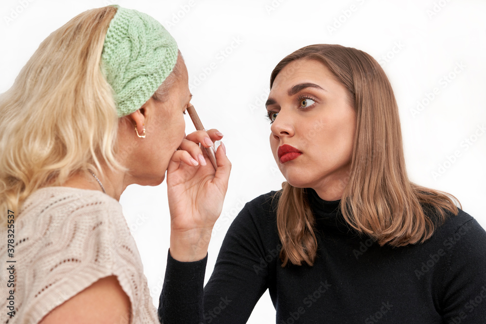 TThe girl paints the eyebrows of the woman with a cosmetic pencil. Isolate TThe girl paints the eyebrows of the woman with a cosmetic pencil. Isolate