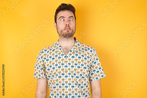 Wallpaper Mural Young man holding pineapple wearing hawaiian shirt over yellow isolated background  making fish face with lips, crazy and comical gesture. Funny expression. Torontodigital.ca